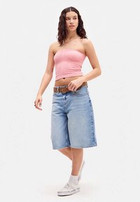 Rožnata top brez naramnic z teksturiranim vzorcem, kombiniran s svetlo modrimi bermudami iz jeansa. Model nosi rjav pas in bele teniske.