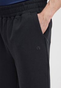Melnas sporta bikses ar elastīgu jostu, sānu kabatām un nelielu melnu logo. Izgatavotas no gluda, elastīga auduma.