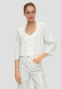 Witte cropped cardigan met driekwartmouwen, textiel van textuur, open voorkant, gecombineerd met een witte V-hals top en lichtgekleurde broeken.