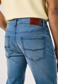 Modre jeans z denima s prileganjem, ki vključujejo dva zadnja žepa, kontrastne šive in rjav usnjen logotip na pasu.
