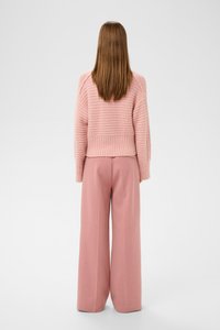 Růžový pletený svetr s žebrovaným lemem a širokými rukávy, v kombinaci s růžovými kalhotami s vysokým pasem a širokými nohavicemi, z pohledu ze zadu.