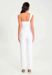 Combi-short blanche avec un dos structuré, des jambes larges et une seule bretelle ornée d'une chaîne. Présente une fermeture éclair dans le dos.