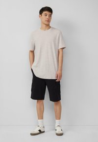 Jasnoszara heatherowa koszulka z krótkim rękawem, zestawiona z czarnymi szortami cargo z bocznymi kieszeniami. Białe sneakersy z czarnymi akcentami.