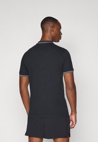 Svart polo-skjorte med korte ermer, med en kontrasterende hvit stripe på kragen og ermeender, laget av teksturert stoff.