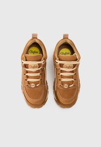 Hnedé semišové tenisky s polstrovaným golierom, béžovými šnúrkami a žltým logom na vložke. Výrazné šitie a textúrovaná podrážka.