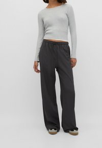 Graues, geripptes Langarmshirt mit einer figurbetonten Silhouette, kombiniert mit locker sitzenden dunkelgrauen Hosen mit elastischem Bund und hellen Kontrastakzenten.