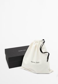 Borsa in cotone bianco con cordino nero e logo stampato, posizionata accanto a una scatola di cartone nera con coperchio, etichettata Massimo Dutti.