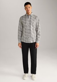 Hemd mit Knopfverschluss und monochromem abstraktem Muster, aus strukturierter Baumwolle, mit langen Ärmeln und klassischem Kragen, kombiniert mit schwarzen Hosen.