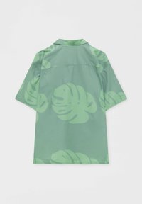 Kurzärmeliges Hemd aus hellgrünem Stoff mit großen, dunkelgrünen Monstera-Blattmustern. Verfügt über einen Camp-Kragen und eine gerade Rückenpasse.