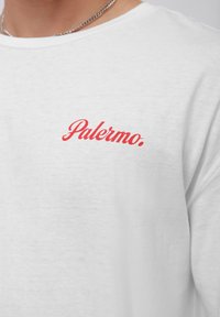 Hvid bomulds t-shirt med rødt kursiv tekst, der står "Palermo." Korte ærmer og rund halsudskæring med en glat tekstur.