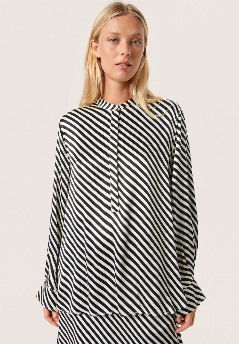 Zwart-wit gestreepte blouse met een hoge kraag, lange mouwen en geplooide manchetten. Heeft een verticale knopenlijst aan de voorkant.