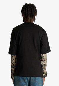 Maglietta nera in cotone vista da dietro, con maniche corte e vestibilità comoda, con maniche lunghe a strati e fantasie visibili sotto.