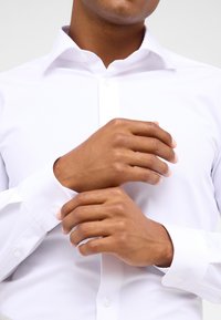Witte overhemd met lange mouwen en knoopmanchetten, met een klassieke kraag en gladde stof, netjes passend rond de hals en polsen.
