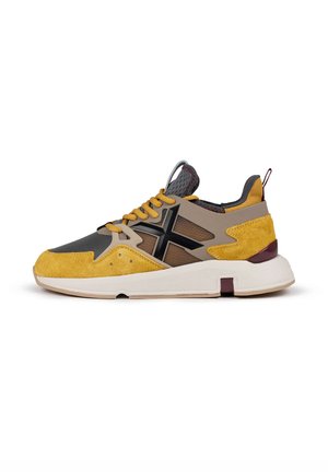 Zapatilla con un upper de ante amarillo, secciones de malla gris, una entresuela beige y acentos negros. Presenta cordones redondos y una pestaña en la parte posterior.