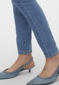 Modre skinny jeans iz денима v kombinaciji z svetlo modrimi slingback čevlji s koničastimi prsti in tankim peto. Odkriti gležnji z tetovažo.