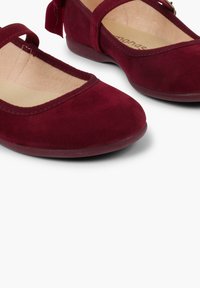 Ballerine in suede bordeaux con punta rotonda, cinturino alla caviglia e morbida fodera beige. Texture liscia con finitura opaca.