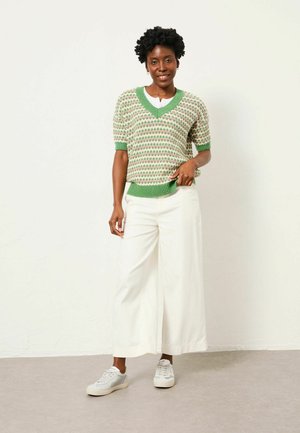 Green and white patterned knit sweater with short sleeves. Paired with wide white trousers and gray sneakers, showcasing a relaxed fit.