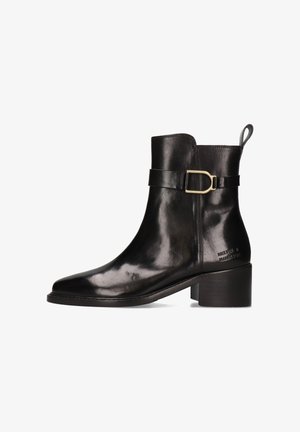 Bottine en cuir noir avec un bout rond, un talon moyen et une sangle latérale avec une boucle en métal. Texture lisse avec un éclat subtil.