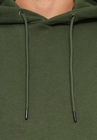 Felpa verde oliva con tessuto texturizzato, cordini regolabili con estremità in metallo nero e dettaglio ravvicinato del collo.