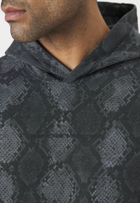 Felpa grigia scura con motivo a pelle di serpente testurizzato, con cappuccio e logo "Jordan Sport" sul davanti. Tessuto di superficie liscia.