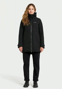 Black zip-up jacket with a high collar, front pockets, and a relaxed fit. Paired with black pants and sturdy black boots.