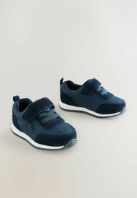 Marineblaue Sneaker aus Stoff und Wildleder, mit einem Klettverschluss, strukturierten Paneelen und einer weißen Gummisohle mit einem gemusterten Profil.