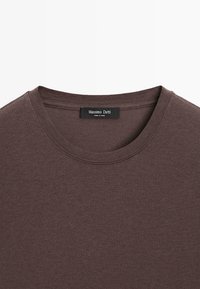 Brun t-shirt med korte ærmer lavet af blødt bomuldsstof. Har en rund halsudskæring og en sort label med "Massimo Dutti" ved kraven.