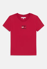 Rød bomulls t-skjorte med korte ermer og rund hals. Har en liten, glitrende logo detalj i midten. Glatt tekstur.