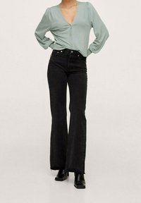 Jasnozielona bluzka z długim rękawem, głębokim dekoltem w kształcie litery V i guzikami; zestawiona z czarnymi rozszerzanymi dżinsami. Całość dopełniają czarne botki za kostkę.