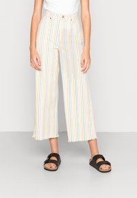 Un pantalon cropped à jambe large avec des rayures verticales multicolores en jaune, bleu et vert. Fabriqué en tissu léger avec un ourlet effiloché.