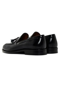 Mocassins en cuir noir avec une finition lisse, dotés de coutures décoratives et d'accents de gland. Talons bas avec des orteils arrondis.