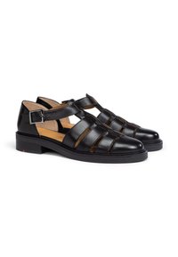 Black leather sandals with cut-out strap design, adjustable ankle buckle, low block heel, and smooth texture.