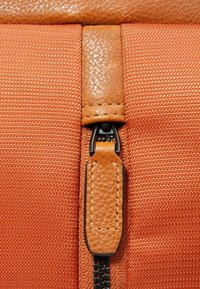 Borsa di tessuto arancione con cerniera in pelle testurizzata, caratterizzata da una finitura liscia e cuciture nere a contrasto sulla cerniera.