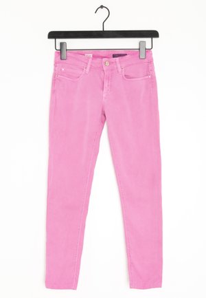 Jean skinny rose avec une texture lisse, cinq poches et une fermeture à bouton en métal. Suspendu à un cintre en plastique noir.