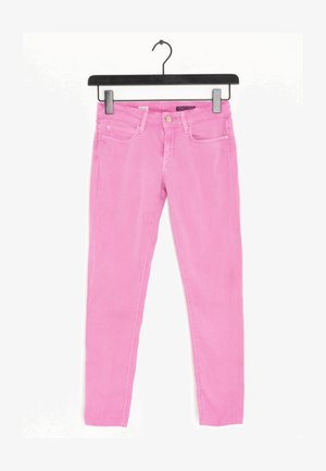 Jeans ajustados rosa con textura suave, cinco bolsillos y cierre de botón metálico. Suspendidos de una percha de plástico negra.