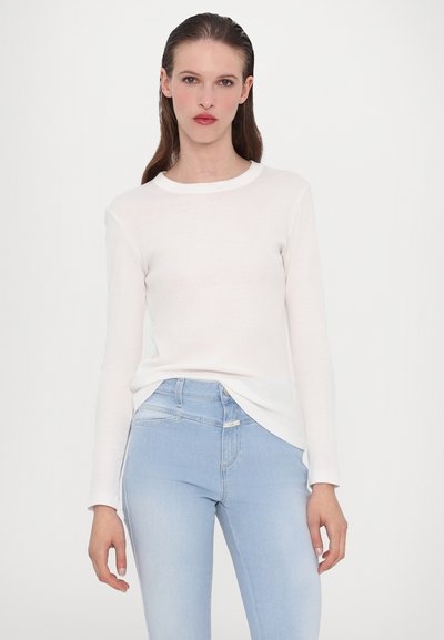 Langermet hvit topp i myk stoff, rund halsutskjæring, kombinert med lyseblå, tettsittende jeans med middels livhøyde og subtile sømdetaljer.
