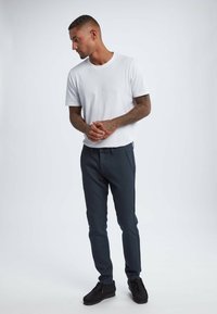 White short-sleeve t-shirt paired with dark gray slim-fit trousers and black shoes. Smooth fabric, minimalist design, no visible patterns or logos.