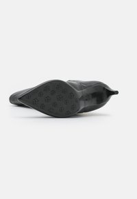Zapato de tacón alto negro con punta afilada, parte superior lisa, tejido texturizado y suela de goma con diseños de flores.