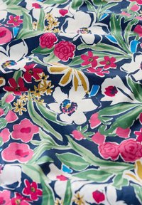 Bombažna tkanina s cvetličnim vzorcem, ki vsebuje rožnate, rdeče, rumene in modre cvetove na temno modri podlagi; gladka tekstura z živahnimi barvami.