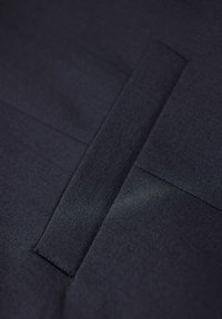 Ciemnoniebieska tkanina o gładkiej strukturze z precyzyjnymi szwami i prostokątnym detalem, tworząca minimalistyczny design.