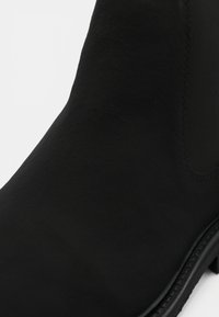 Bottine noire à finition mate lisse avec des détails cousus le long du côté et du bord de la semelle.