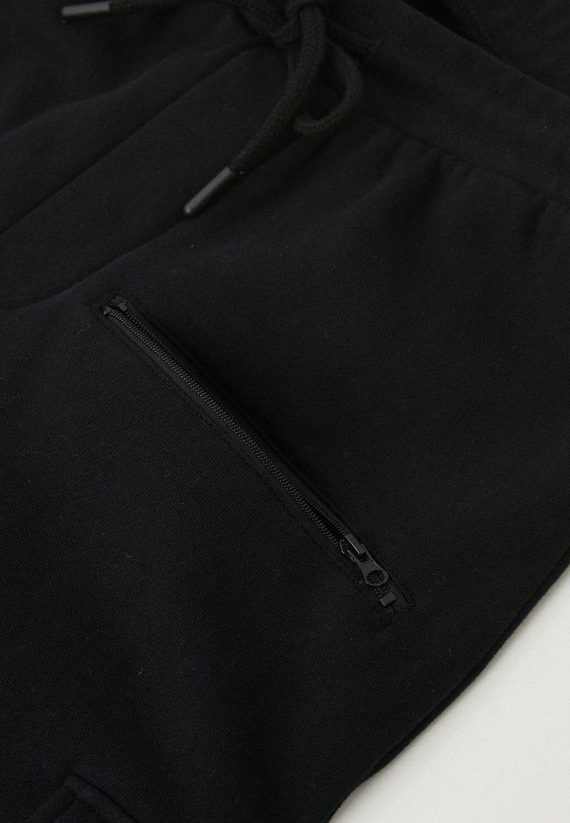 Čierne joggingové nohavice vyrobené z mäkkej látky, s predným vreckom na zips na stehne a nastaviteľnými šnúrkami v oblasti pása.
