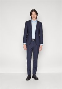 Marineblauer Anzug aus gewobenem Stoff, bestehend aus einem taillierten Blazer mit Reverskragen, kombiniert mit passenden Hosen und einem hellblauen Hemd.