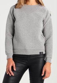 Pull-over gris clair avec texture côtelée, encolure ronde et coutures latérales. Poignets et ourlet ajustés avec détails de logo en bas.