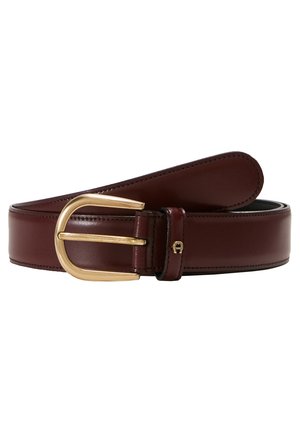 Bordeaux leren riem met een gladde textuur en een grote gouden metalen gesp. Bevat een klein logo-detail op de riem nabij de gesp.