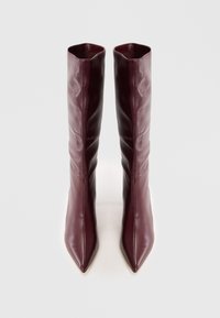Bottes en cuir bordeaux montantes avec un bout pointu, présentant un design élégant et une texture douce, affichant des plis subtils le long de la tige.