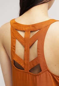 Top arancione senza maniche con un design a incrocio sulla schiena. Realizzato in tessuto morbido, presenta una finitura testurizzata e dettagli aperti tra le spalline.