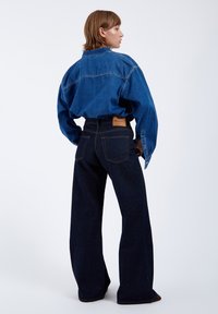 Denim shirt with blue hue, loose fit, and button cuffs; paired with dark blue high-waisted wide-leg jeans featuring back pockets and branding.