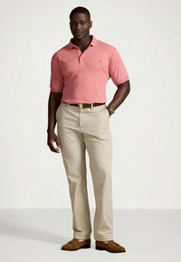 Lys rosa poloshirt kombinert med beige bukser. Skjorten har krage og korte ermer. Brune sko fullfører antrekket.