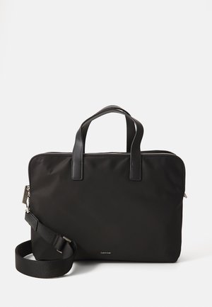 Sacoche d'ordinateur portable noire en nylon avec des poignées en cuir. Elle dispose d'une fermeture éclair et d'une sangle détachable pour plus de polyvalence. Design minimaliste.